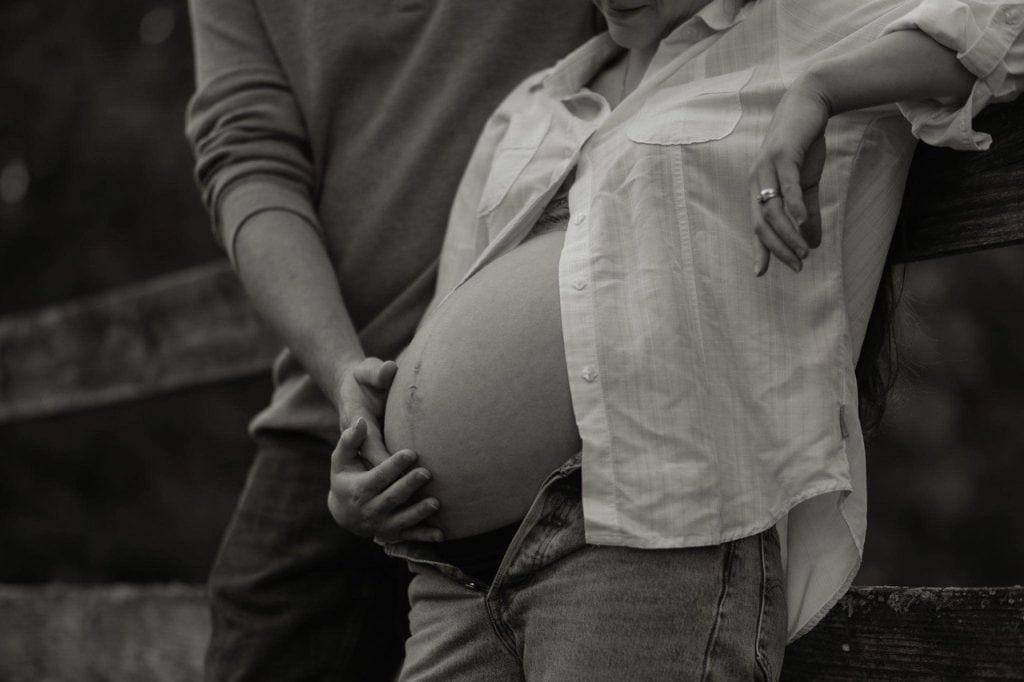 Black and white photo of husband holding his pregnant wife's belly in Maternity Photo Session