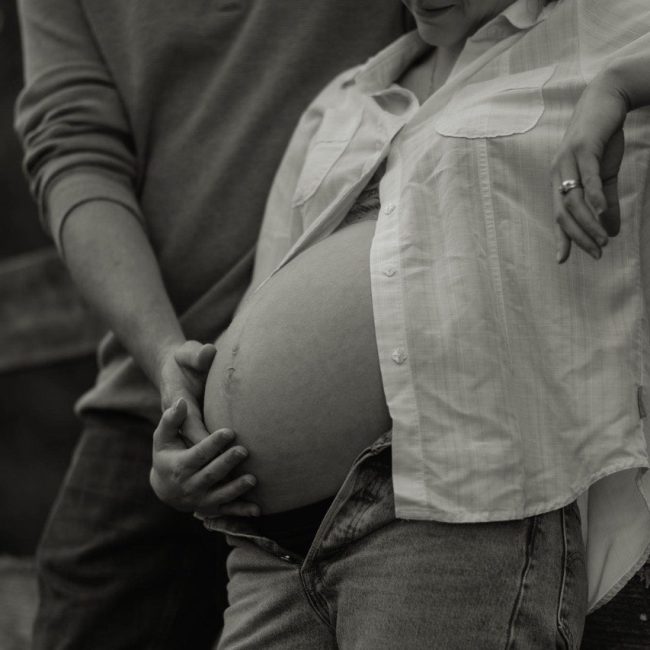 Black and white photo of husband holding his pregnant wife's belly in Maternity Photo Session