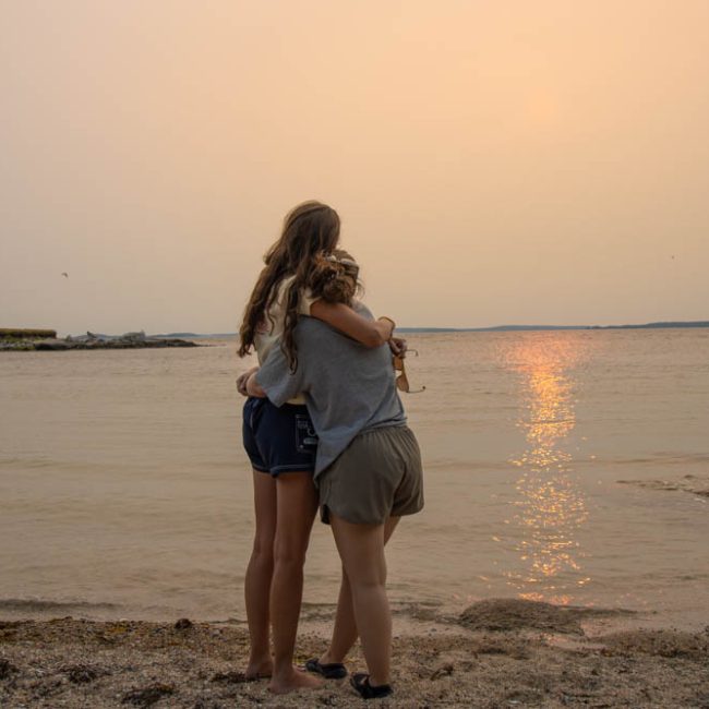 two friends hugging each other while standing on the shore of Lake Jordan in Durham NC - A family photography session with Amelia and Matt Photo