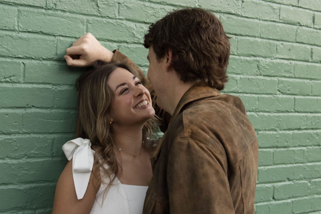 Woman Smiling while looking at her fiance in front of a green wall in City Market in Downtown Raleigh NC - Engagement Session