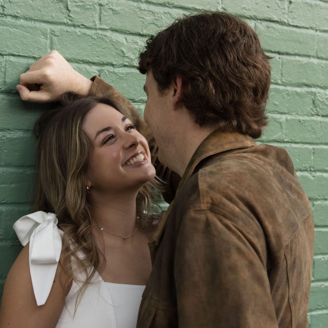 Woman Smiling while looking at her fiance in front of a green wall in City Market in Downtown Raleigh NC - Engagement Session