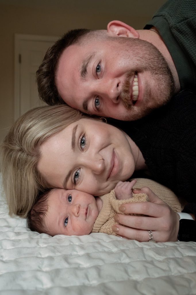 Parents stacking their heads with their newborn baby in bed - newborn at home photography session in Durham NC