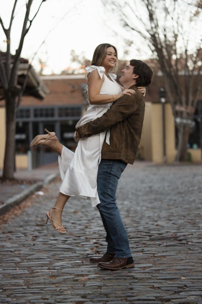Newly Engaged Couple Holding each other in cobblestone street in City Market in Downtown Raleigh NC - Engagement Photographer Raleigh North Carolina