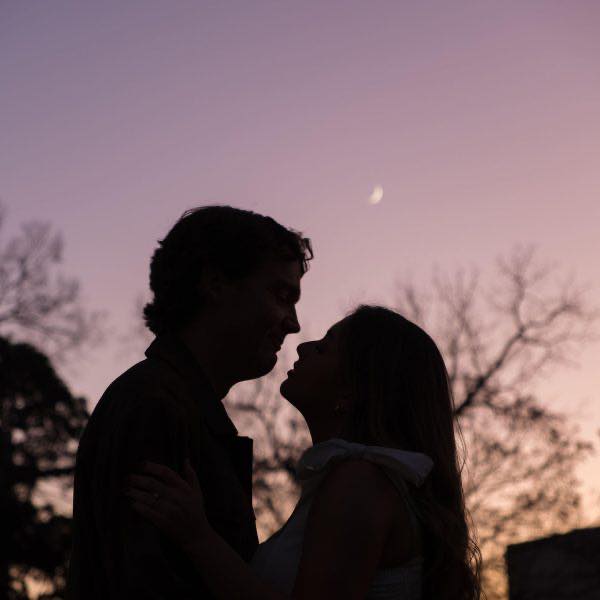 A couple holding each other in an intimate moment during an engagement session in Downtown Raleigh NC with the moon glowing in the background during a sunset