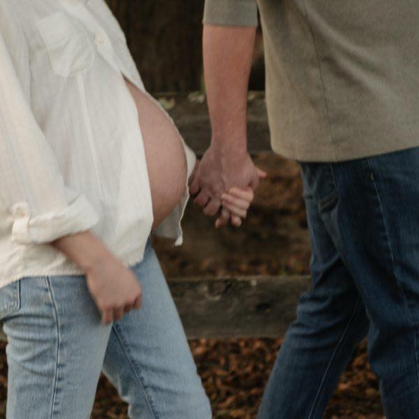 A couple holding hands while walking in front of a fence during a maternity photoshoot in Durham NC with Amelia and Matt Photo
