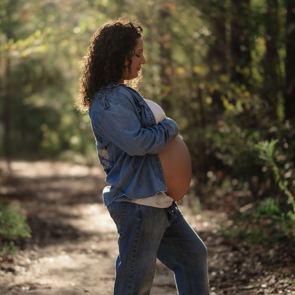 A pregnant mom holding her stomach while posing for Amelia and Matt photo near Jordan Lake in Durham NC for a Maternity Photoshoot pregnant woman walking morning sunlight