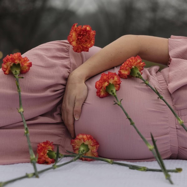 Pregnant mother laying in a field on a blanket for maternity photos with flowers laying around her belly bump