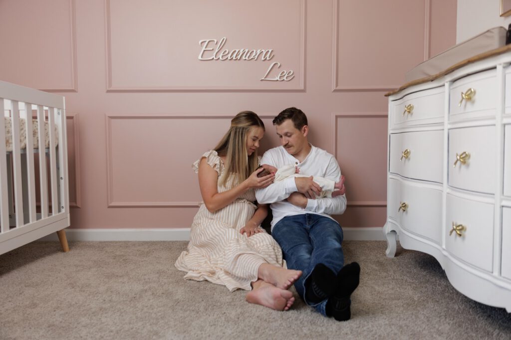 a mom and dad sitting on the floor of their nursery holding their newborn baby during an in-home newborn session