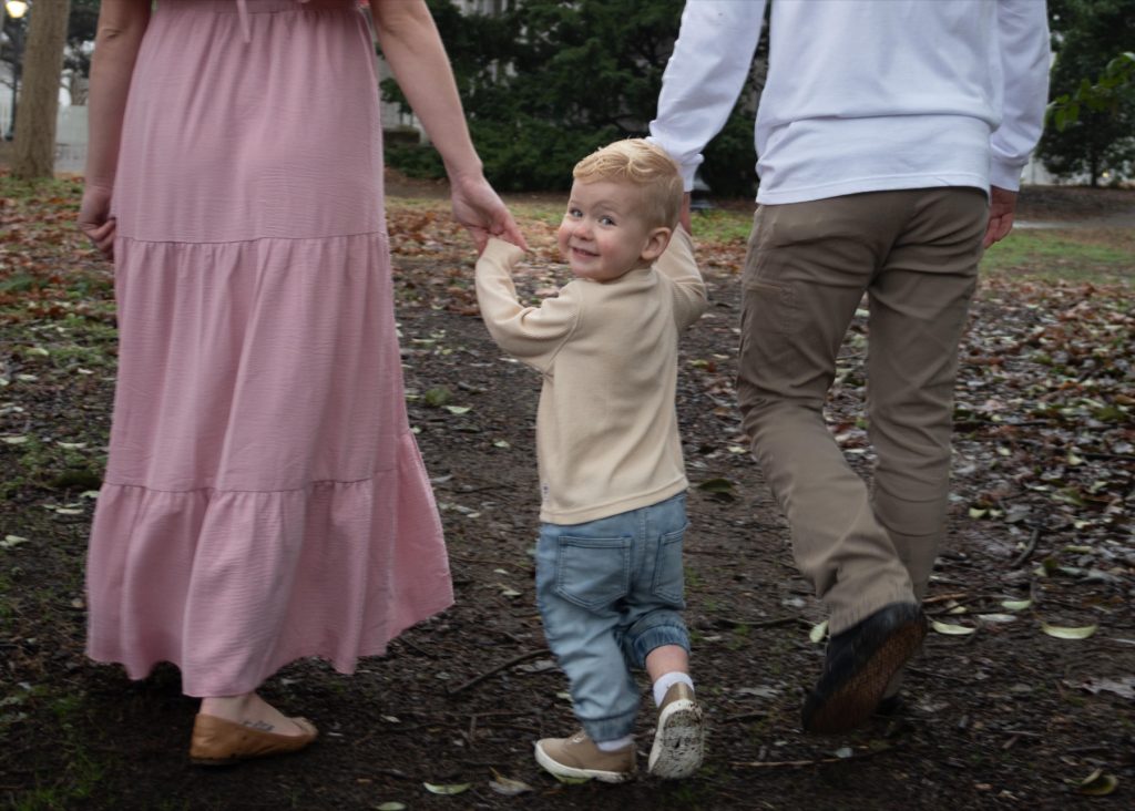 a boy looking back at the camera and smiling while walking with his parents in a family photo session at Oak view park in Raleigh NC