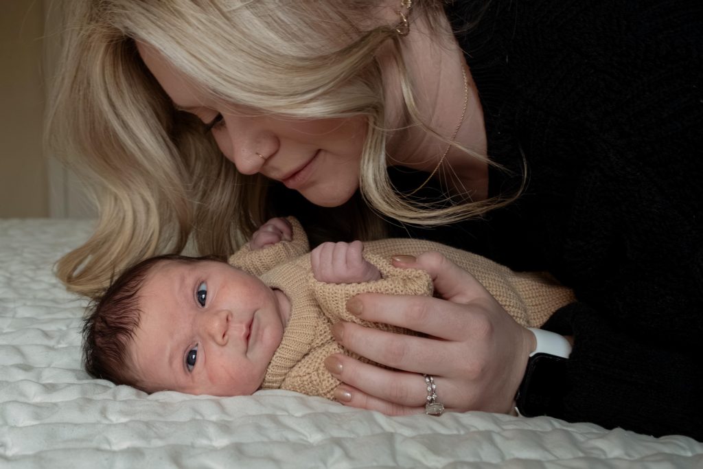 a mom looking at their 1 week old baby that is laying on their bed in a newborn photography session at their home in Durham NC