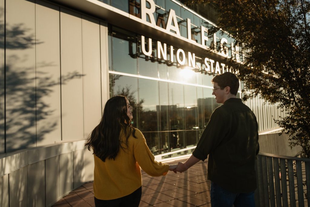 A couple walking into the sun with the Raleigh Union Station Sign in the foreground