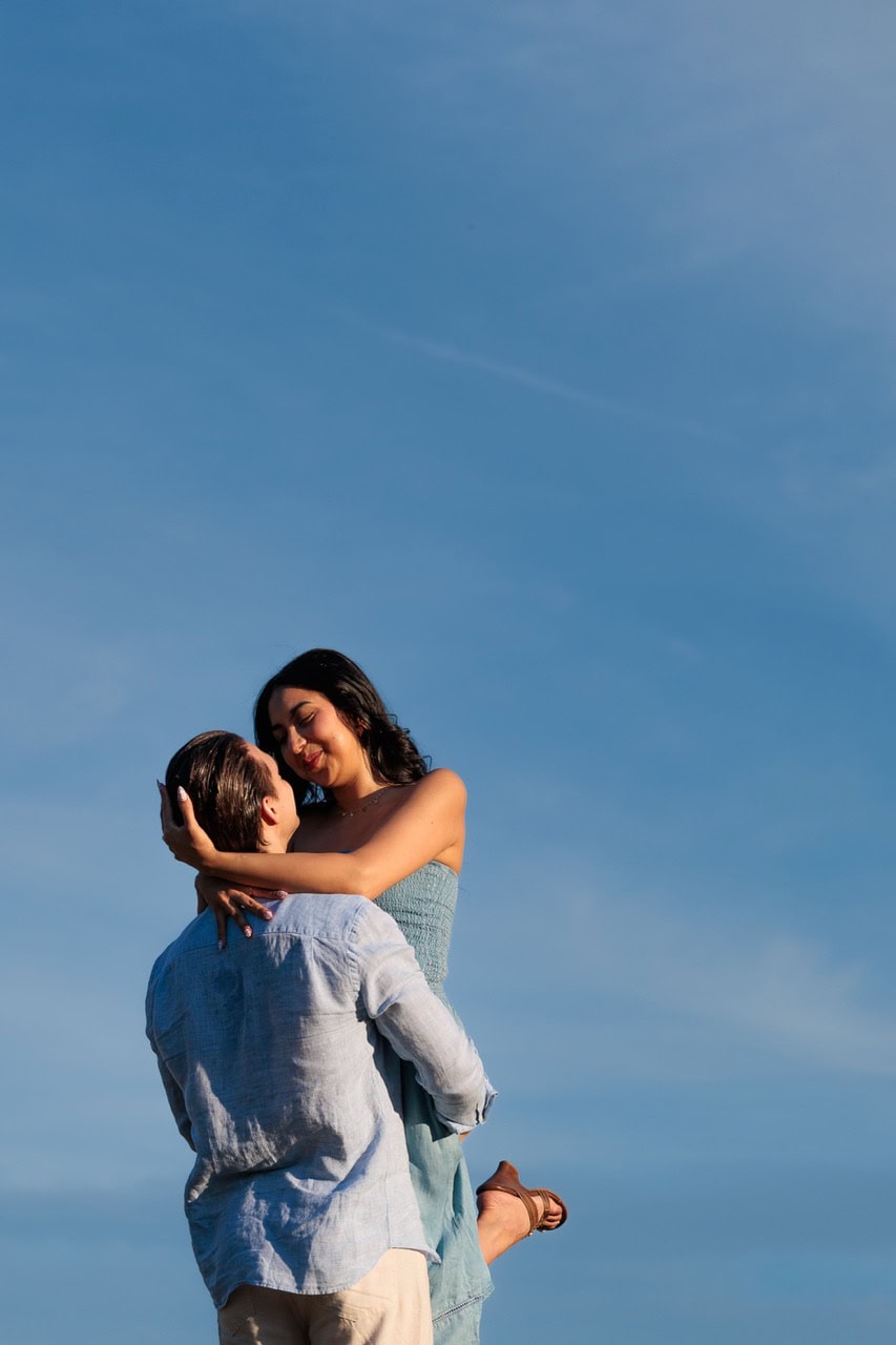 a man holding up his wife with the sky as the background