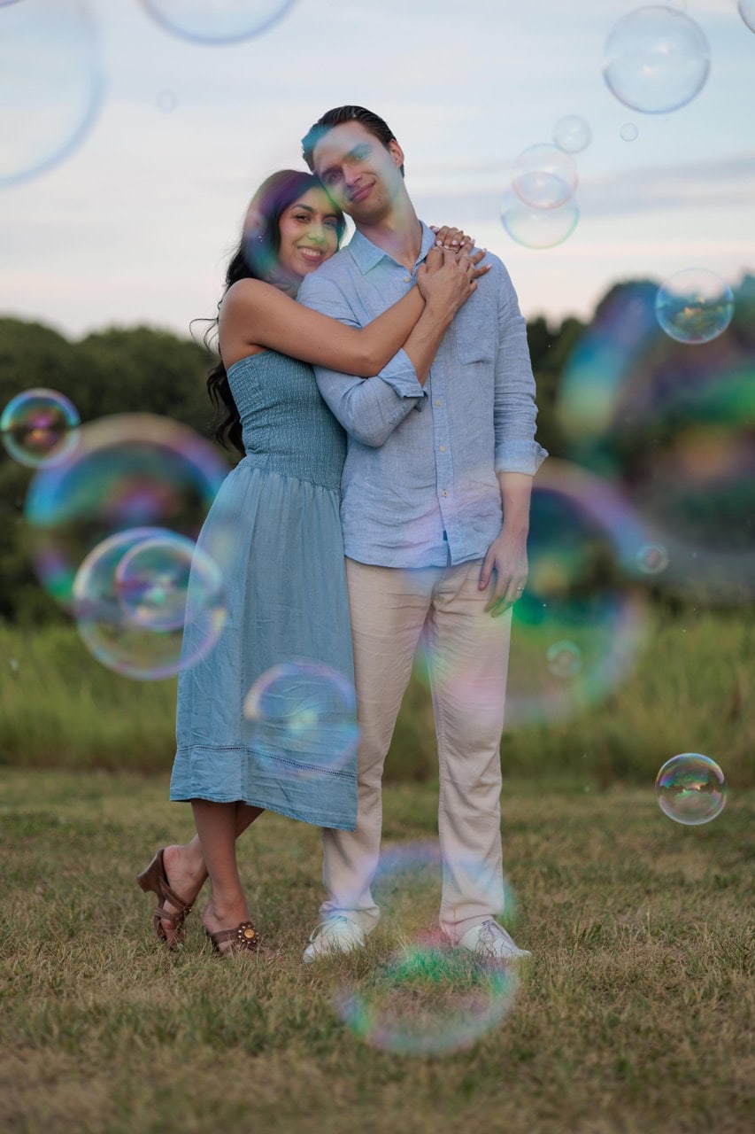A couple posed behind bubble blown by the raleighbubbleman. they are leaning on each other while the golden hour sun sets
