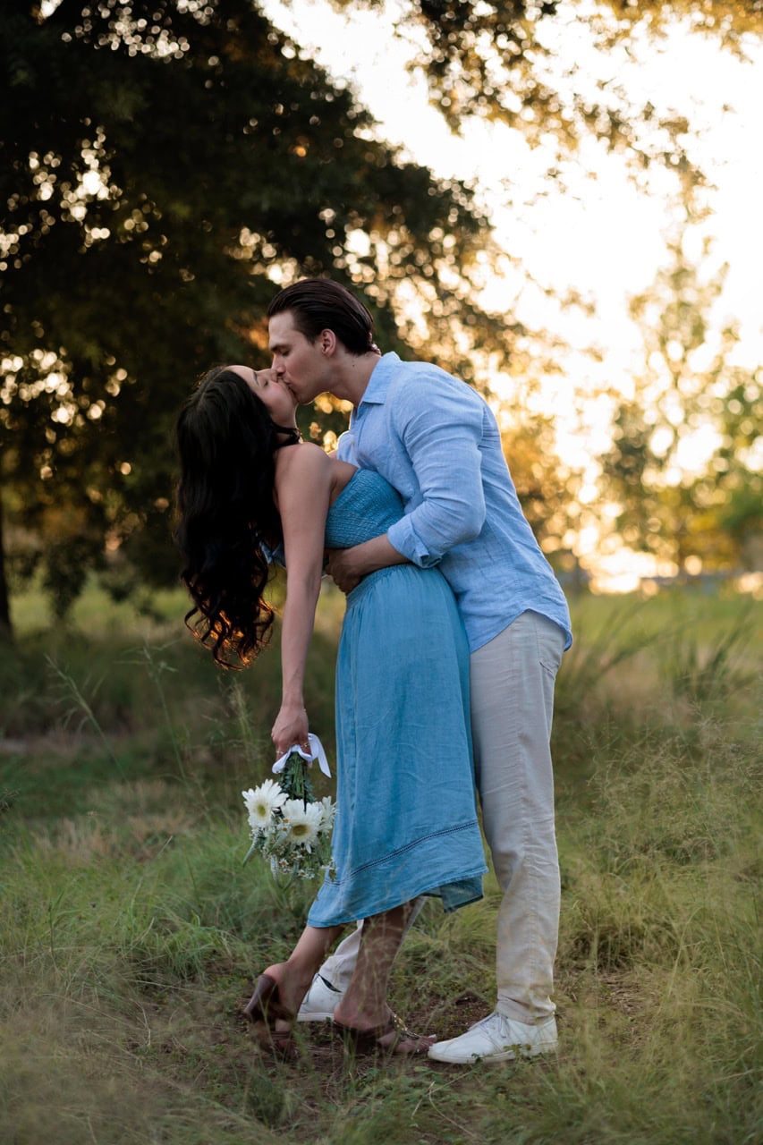 a couple kissing in front of the sunset in a field of tall grass