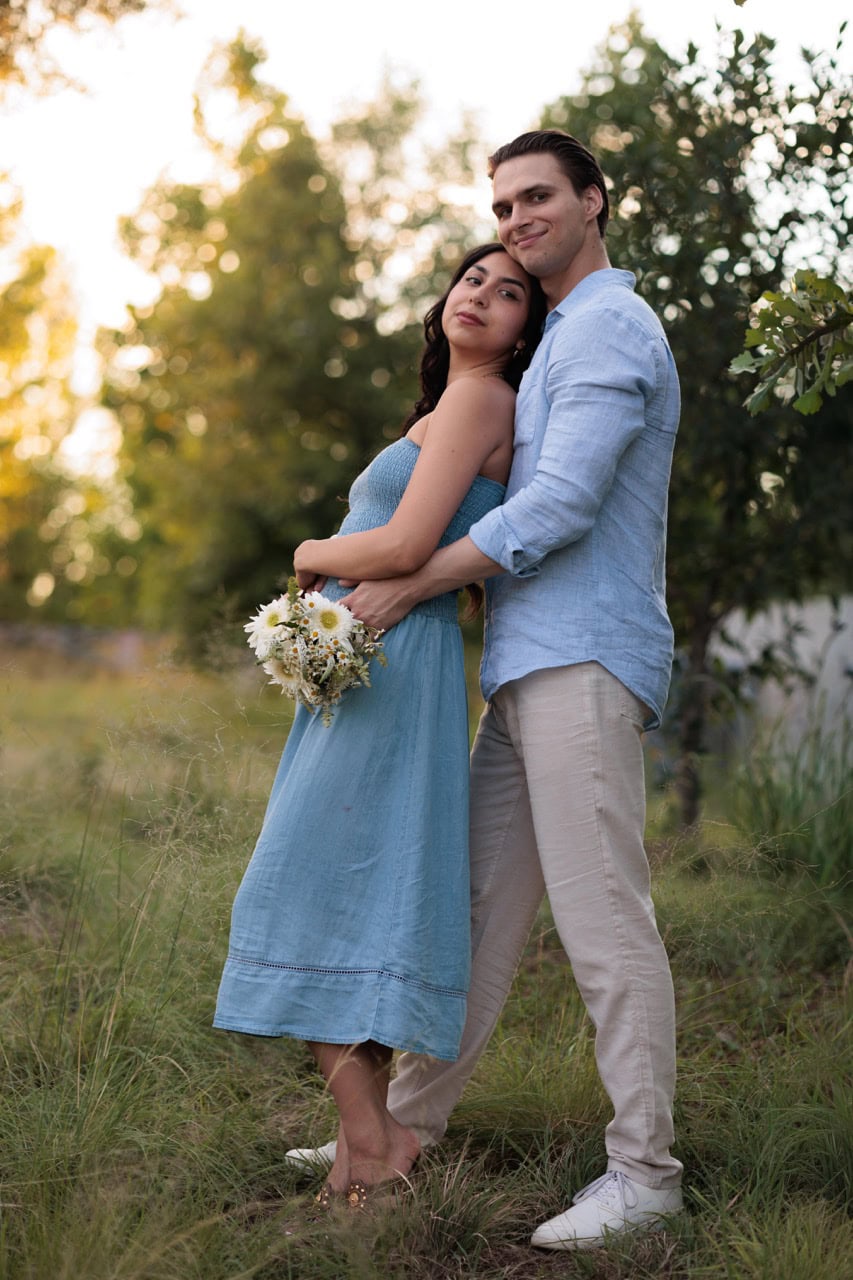a couple posed looking at the camera with the golden sun setting behind them while they stand in tall grass in Raleigh NC