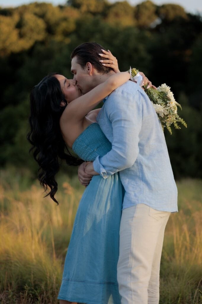 A couple kissing in a field at the NCMA with tall grass in the background and golden hour lighting