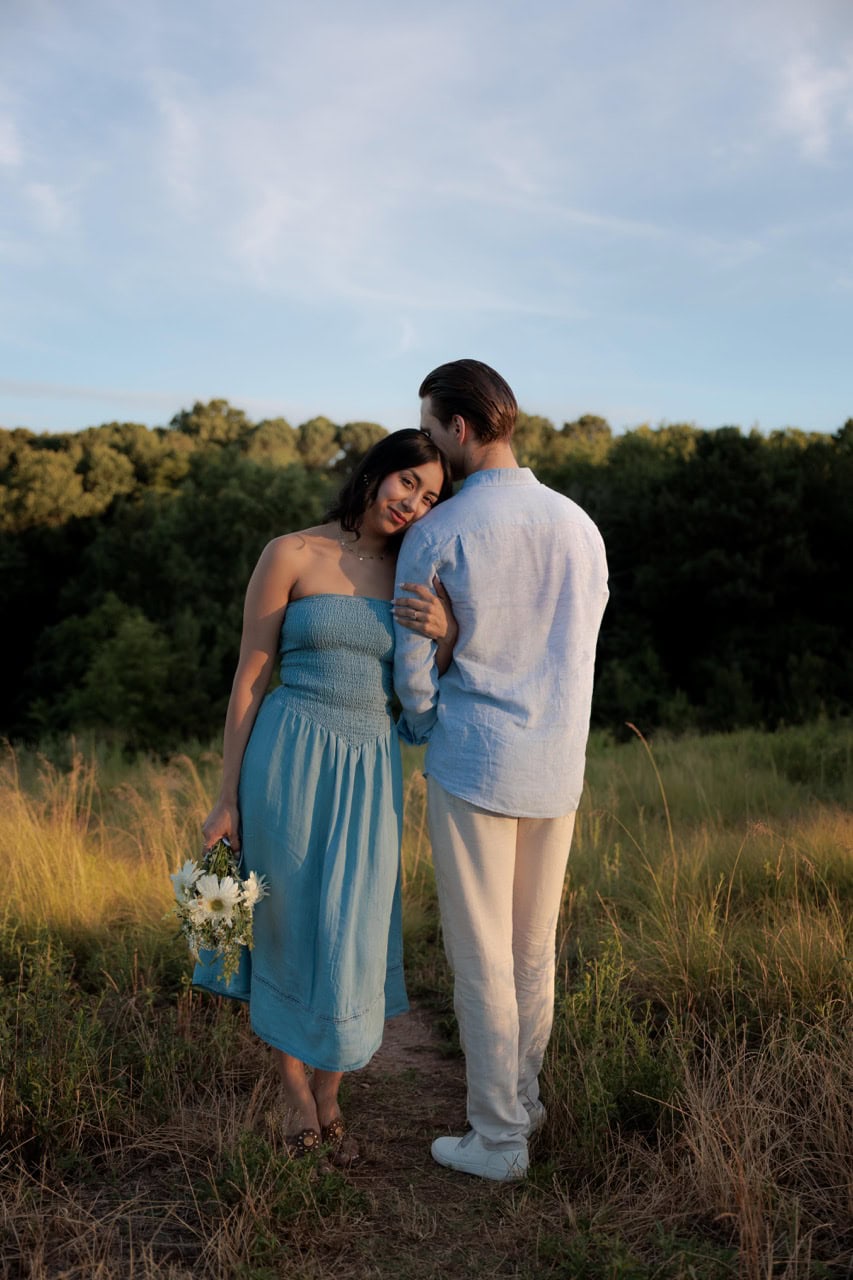 A woman looking into the camera as her husband looks into the distance while the golden hour sun is setting