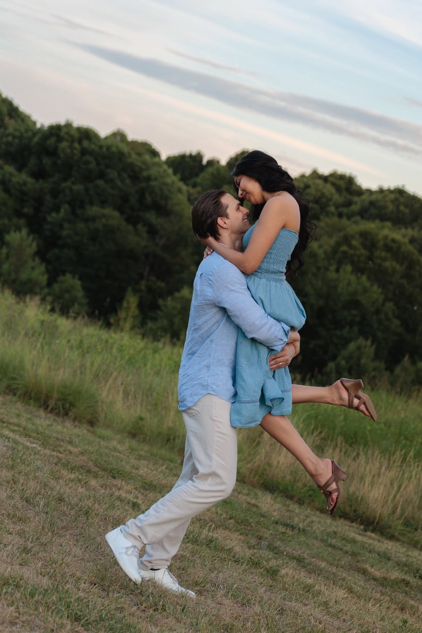 A dutch angle photograph of a man lifting his wife into his arms in front of a filed as they are about to kiss