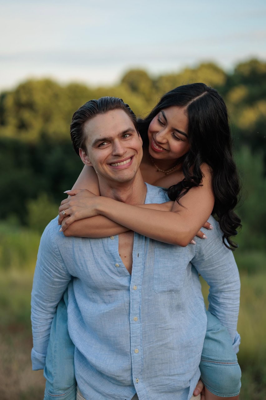 A man holding his wife on his back as they both smirk into the camera during their photoshoot