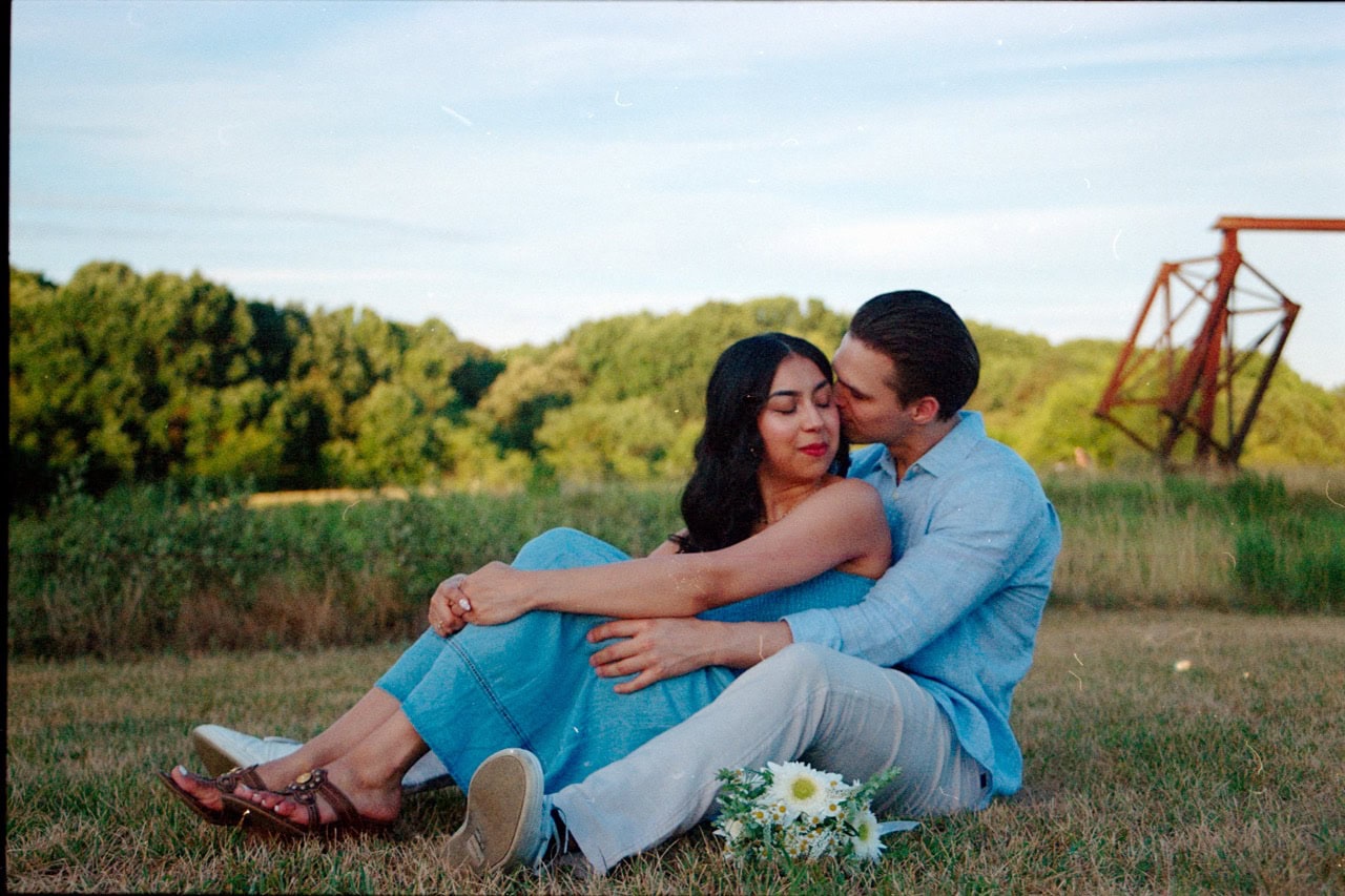 a 35mm film photograph of a couple sitting near art at the NCMA museum grounds in Raleigh. They are sitting amongst tall grass