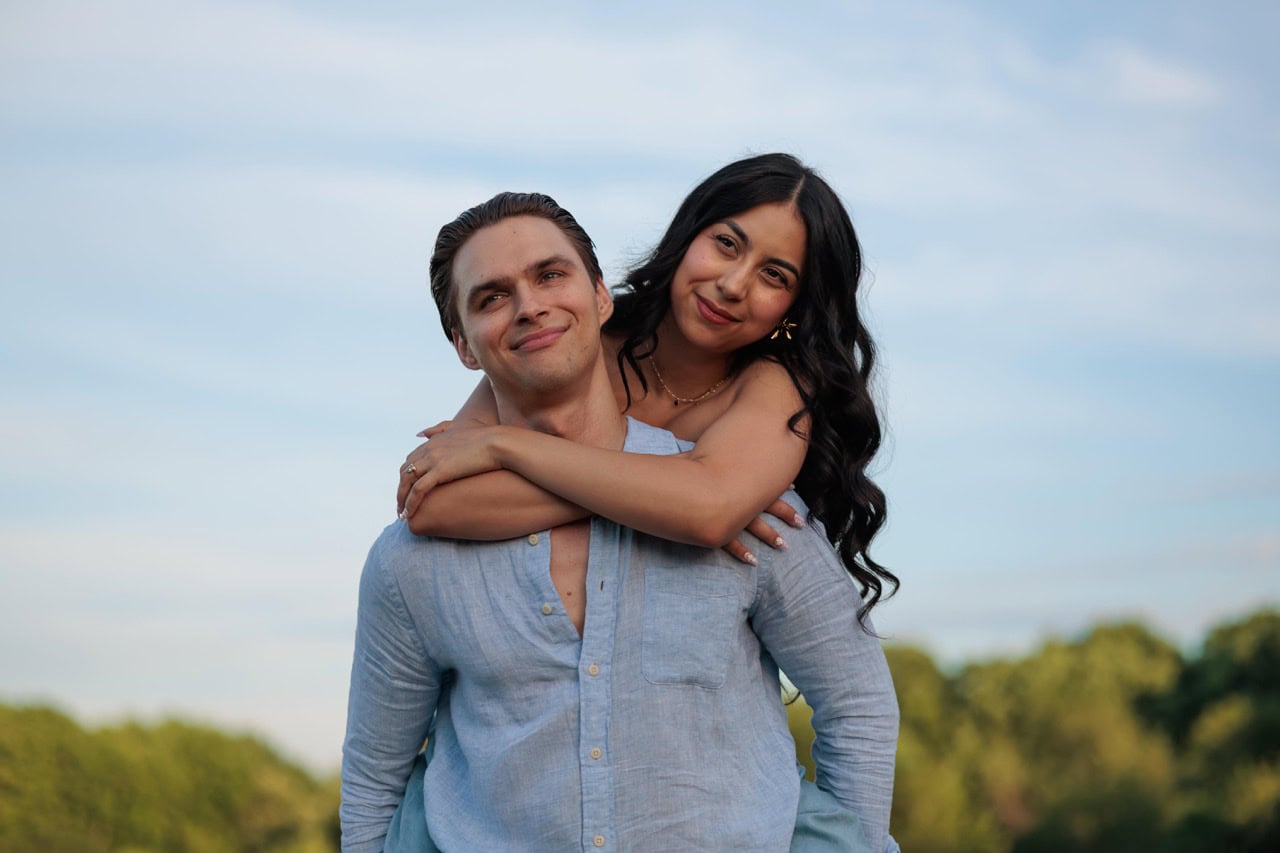 a man carrying his wife on his back during a photoshoot for their anniversary with Amelia and Matt Photo. They are standing with trees in the background as the sun sets and they smirk