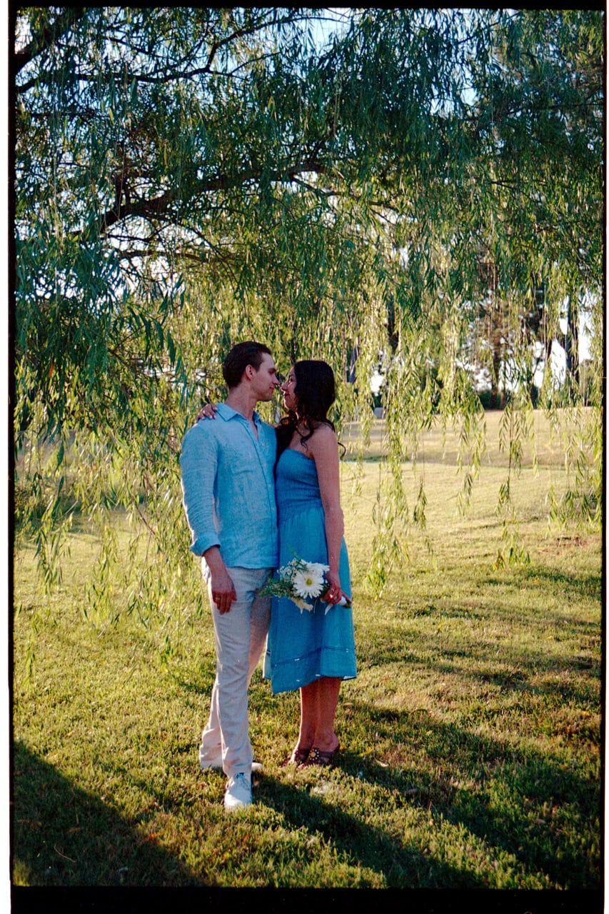 A film photograph of a couple standing in front of a weeping willow on 35mm film taken by Amelia and Matt Photo