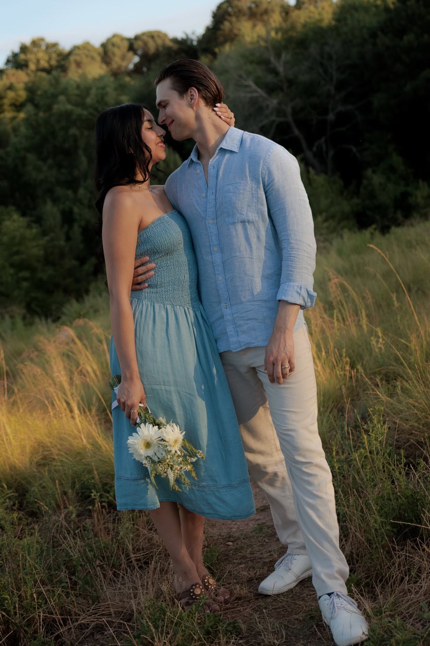 A couple making deep eye contact about to kiss in their couples photography session with Amelia and Matt Photo. She is holding a bouquet of flower as they sand amongst tall grass