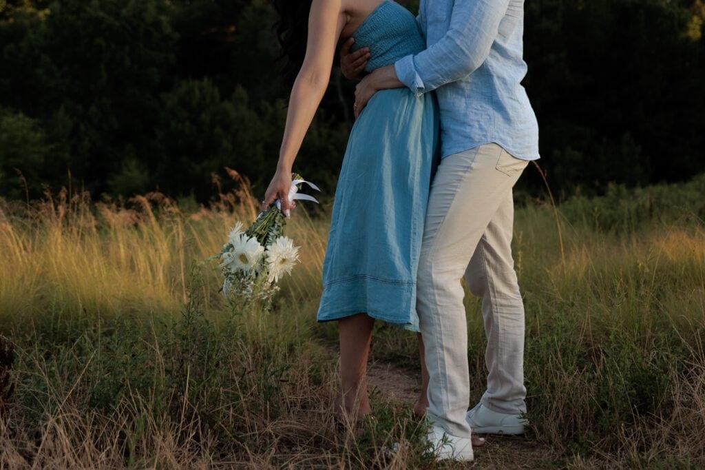 A detail photograph of a couple kissing while she holds a bouquet of white flowers while standing in tall grass at the NCMA in Raleigh NC