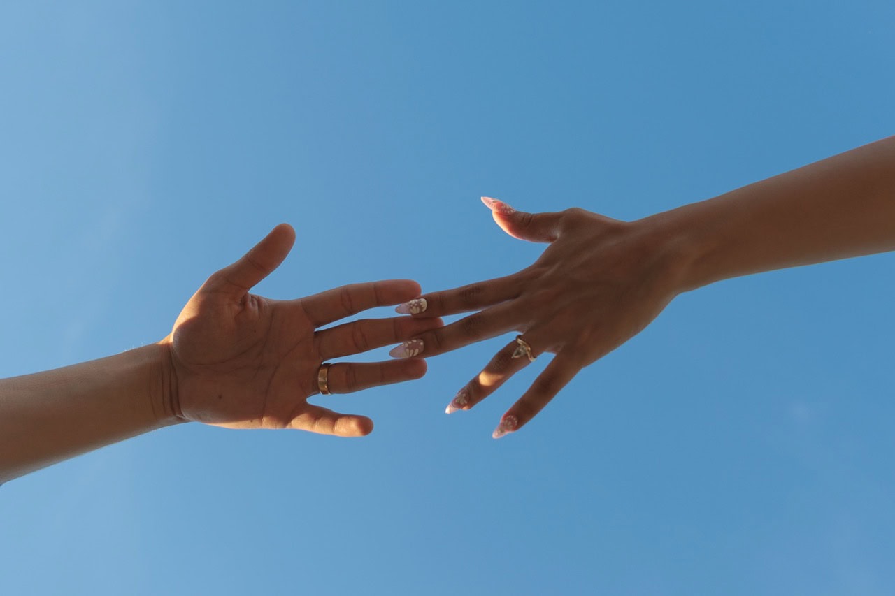 A photo of a couples hands grazing away from each other with the background of the sky. It is very cinematic and artistic