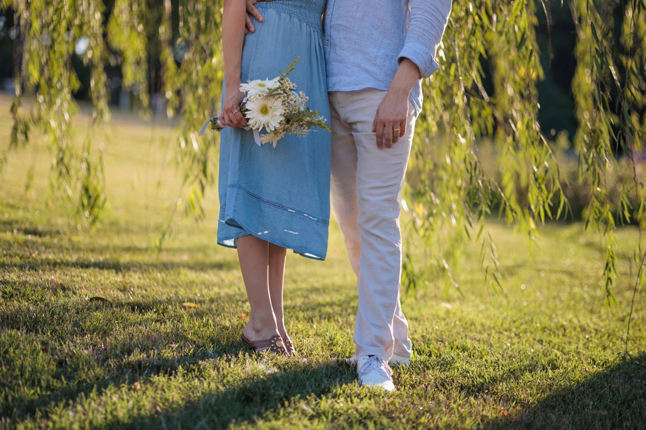 A detail shot of a couple next to each other under a willow tree at the NC museum of art for a photoshoot. she is holding a bouquet of flowers for their anniversary.