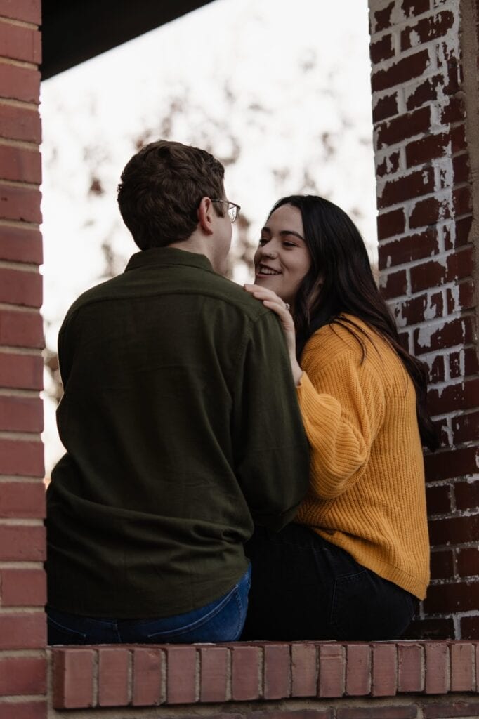 Couple sitting on a brick wall at Barcelona Wine Bar in Downtown Raleigh NC during their engagement session with Amelia and Matt Photo
