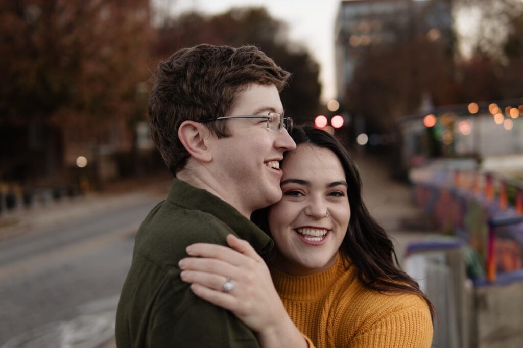 Couple standing on boylan bridge smiling into the camera showing off their new engagement ring.