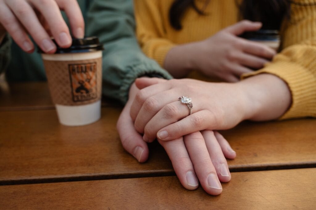 Cup of coffee from sir walter coffee with a couple holding each others hands. She is showing off her engagement ring