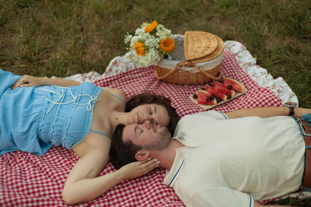 a couple laying on a blanket holding each other with a picnic basket next to them