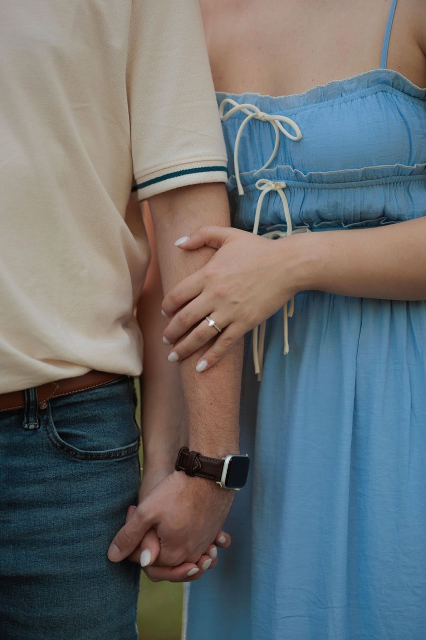 a woman grasping her husbands arm at sunset. a detail shot showing off the ring