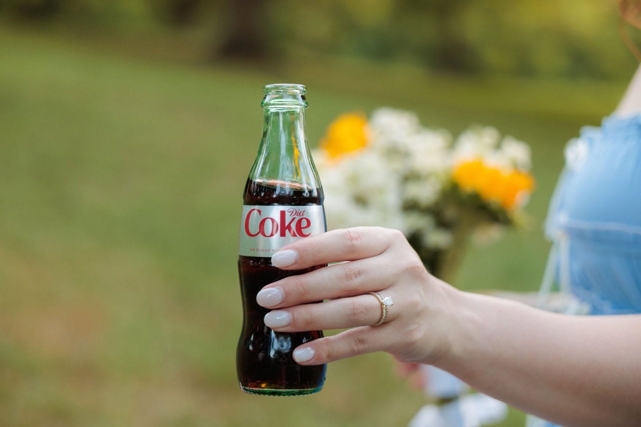 a glass bottle of diet coke in front of some wild flowers
