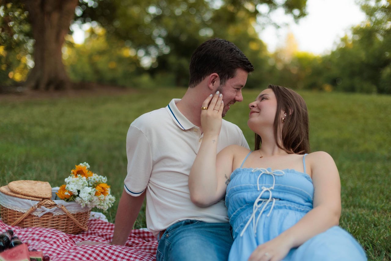 Couple about to kiss while sitting on a picnic blanket on a filed at golden hour