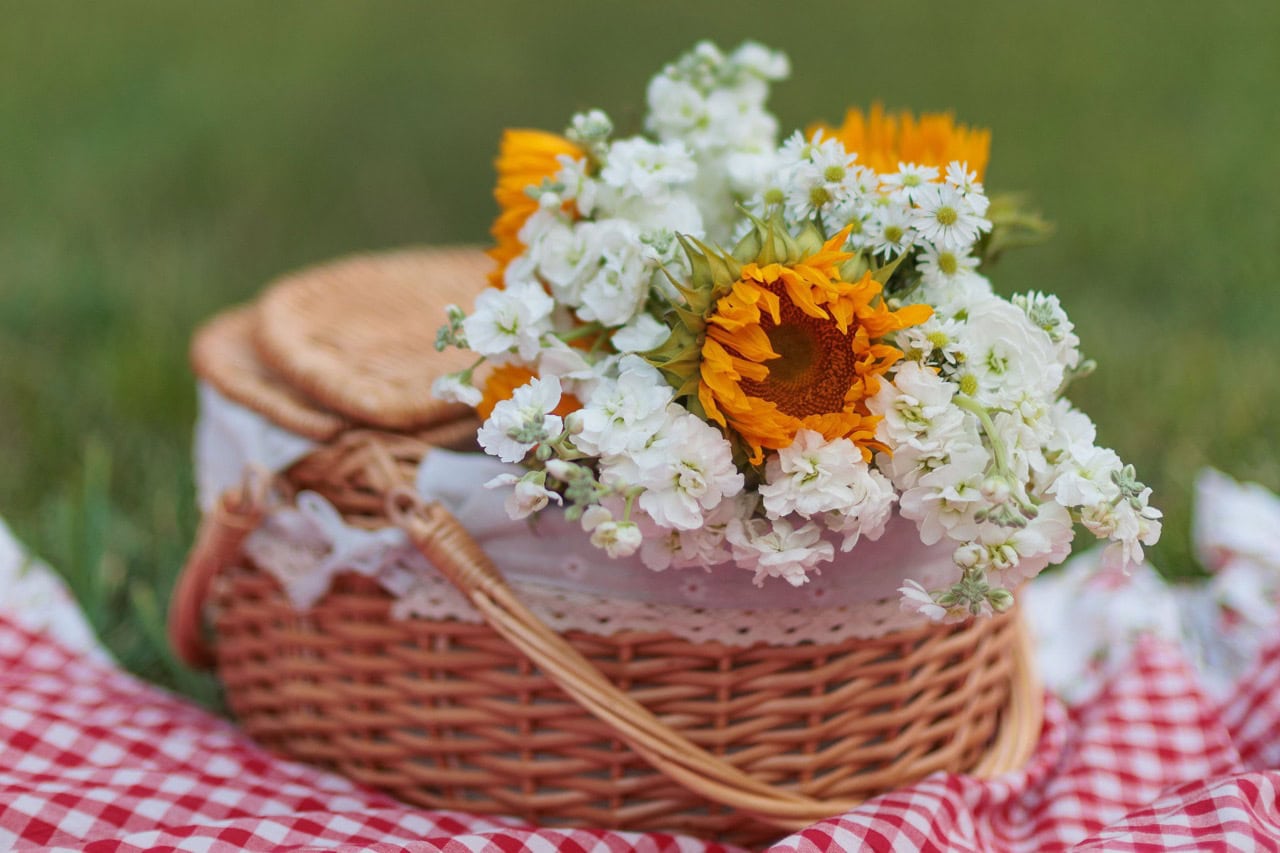 detail photograph of a basket of flowers on a picnic blanket