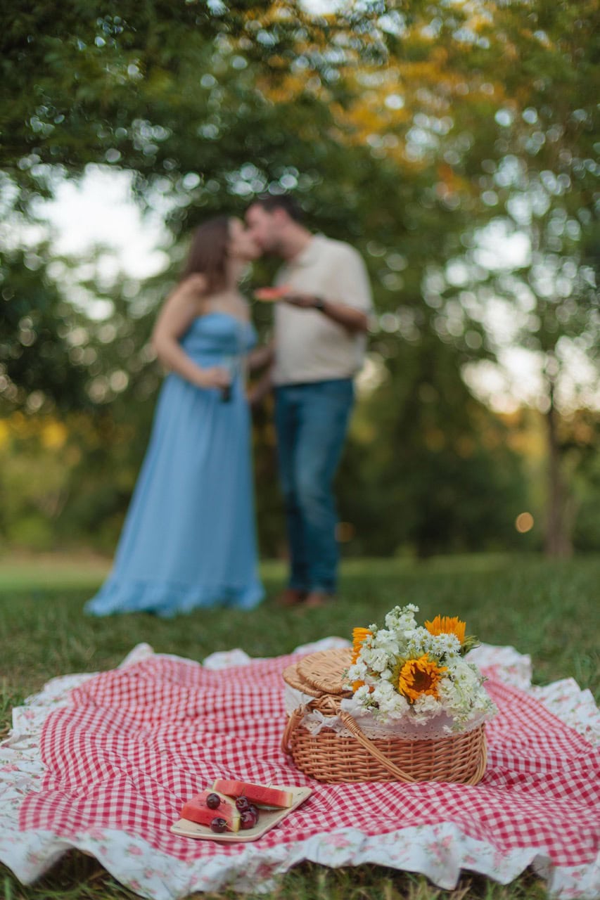 cinematic photo of a picnic with flowers, a basket, checkered blanket and fruit while a couple hold diet coke bottles and kiss