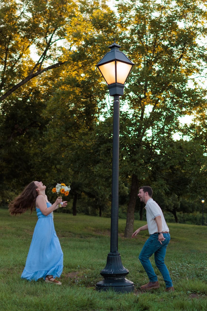 couple chasing each other playfully around a lamp post in front of a field