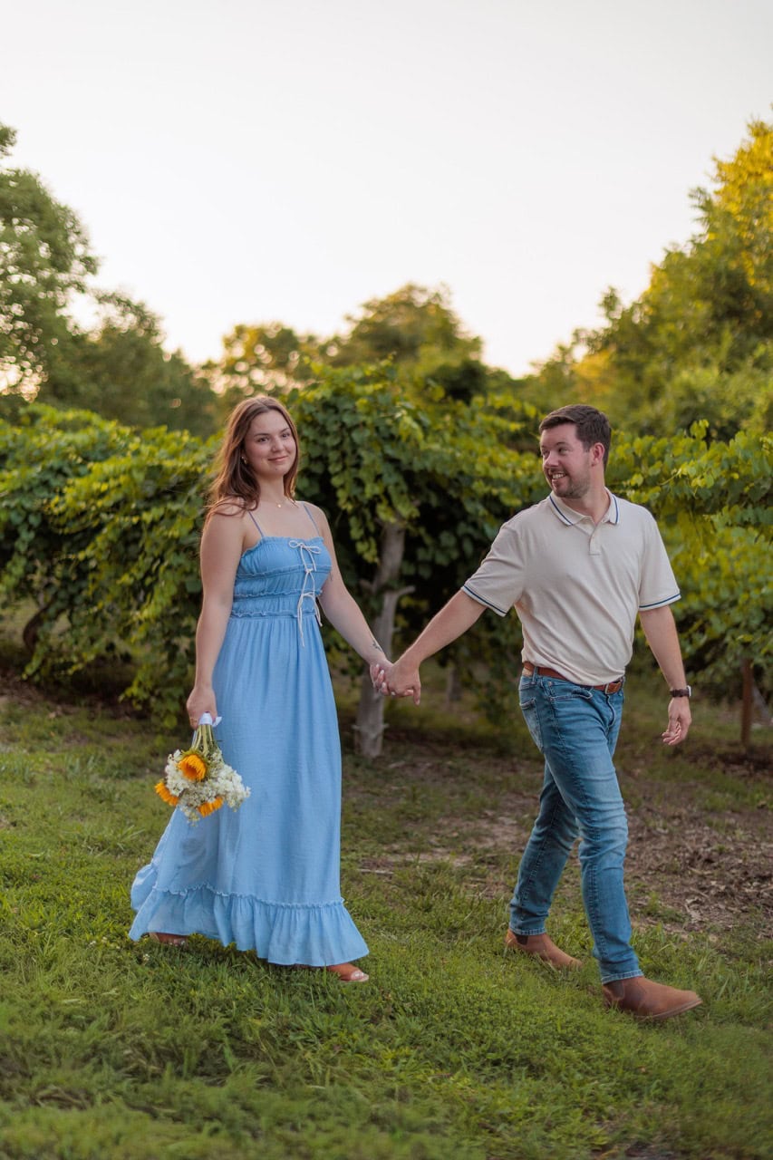couple walking near a vineyard while holding hands at sunset