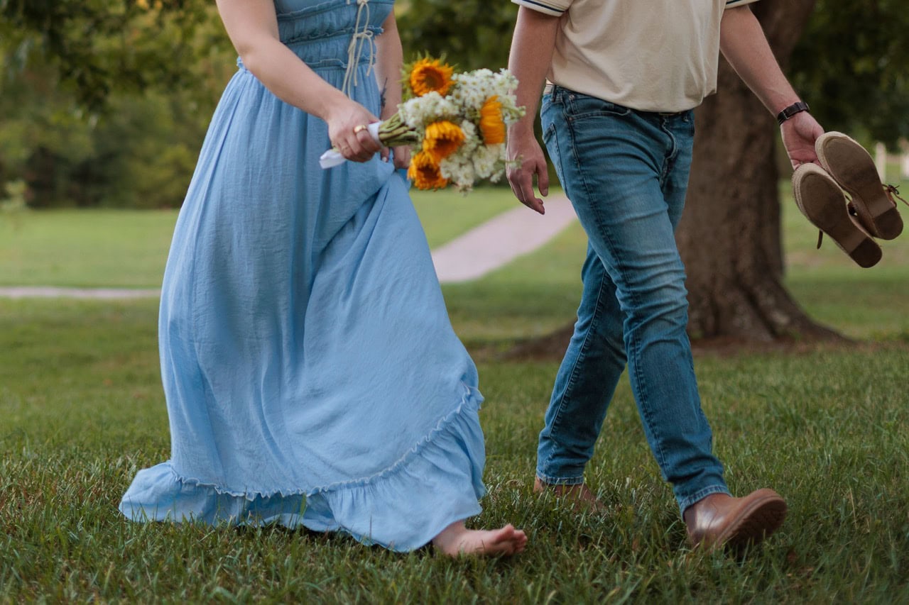 couple holding hands while walking in a field, the woman is wearing a blue dress and flowers