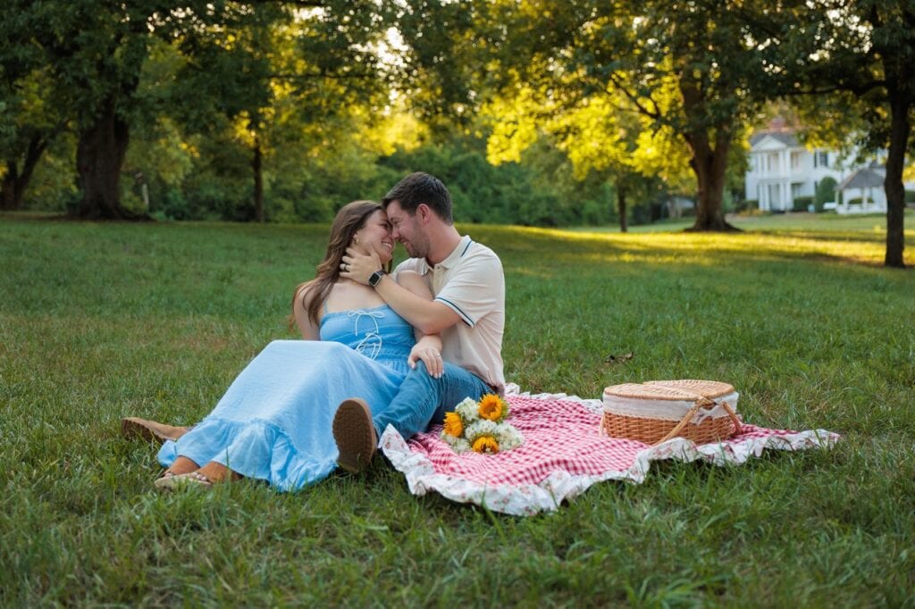couple kissing sitting on a picnic blanket on a field at golden hour in Raleigh NC