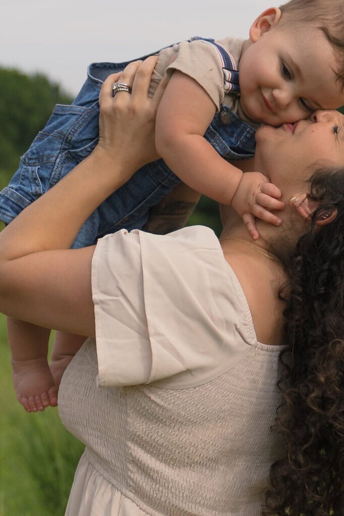  A baby holding his mother while being held and kissed on the cheek during a family photography session