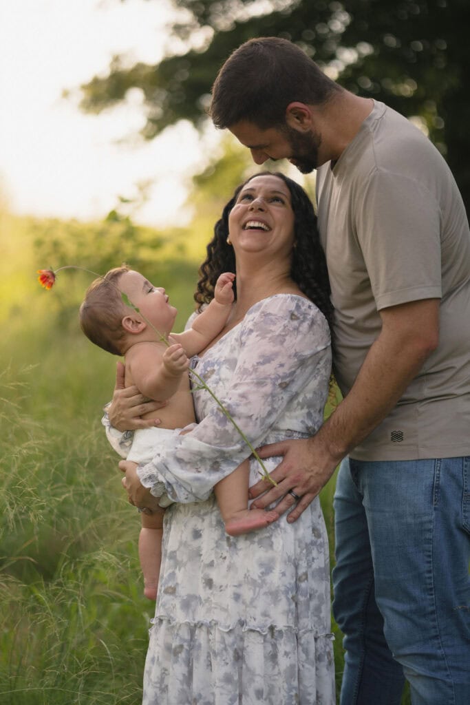 A photograph taken at golden hour of a family holding their 9 month old baby as they look into each others eyes