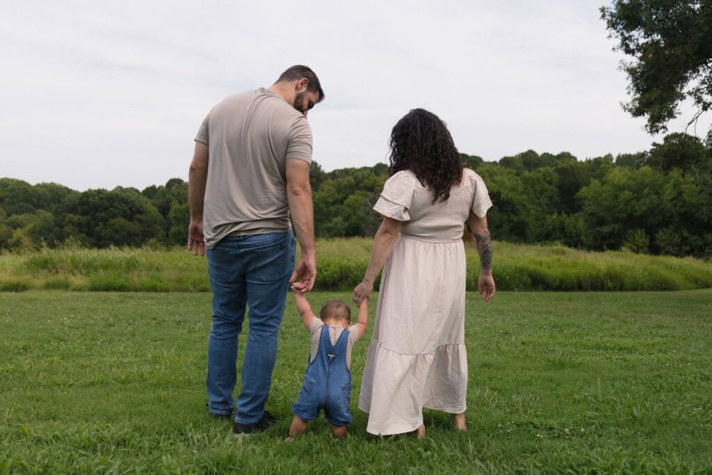 Parents holding their son's hand in a field of tall grass during their Family Photography session with Amelia and Matt Photo