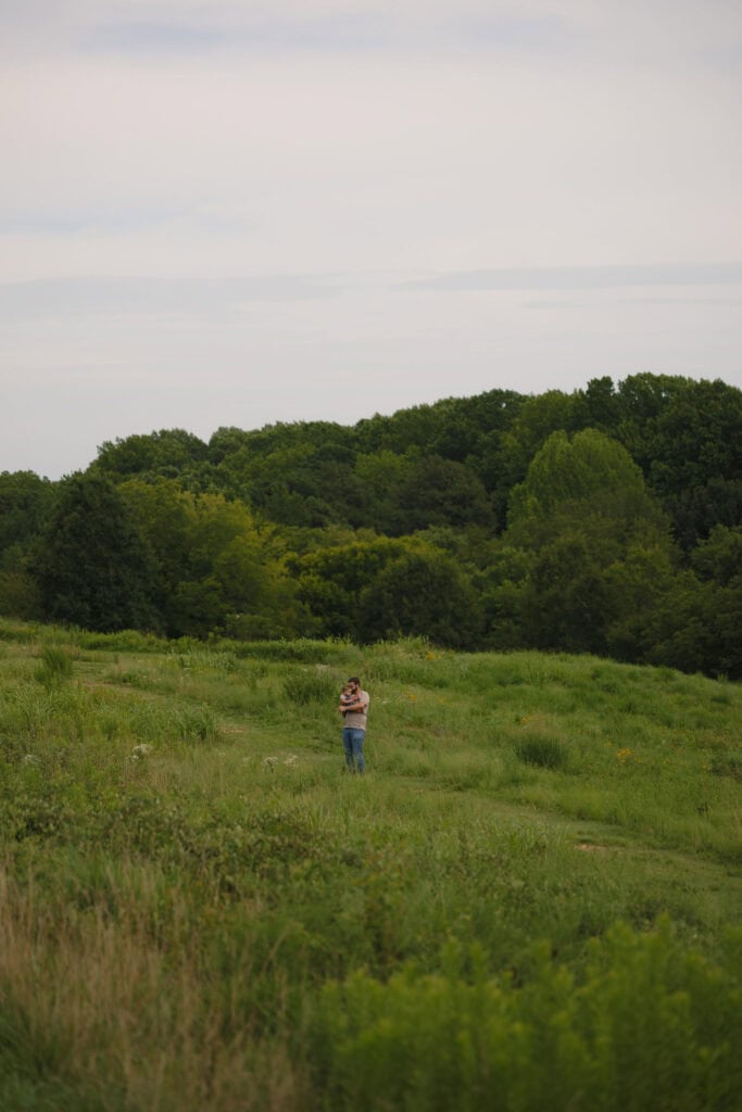 a wide photograph of a father holding his toddler in a field of tall grass in Raleigh NC