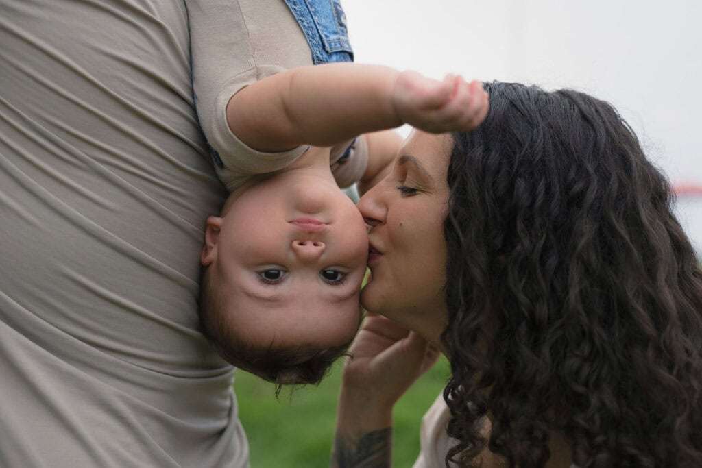 A toddler getting kissed on the cheek by his mother during a family photography sesison