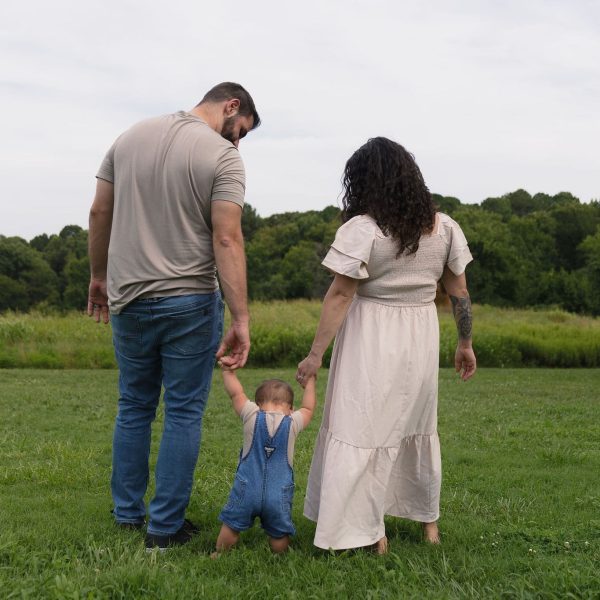 Tyniy_JPEGLI_v1.0_distance4.0_2026-07-27T01:31:54Z Parents holding their son's hand in a field of tall grass during their Family Photography session with Amelia and Matt Photo