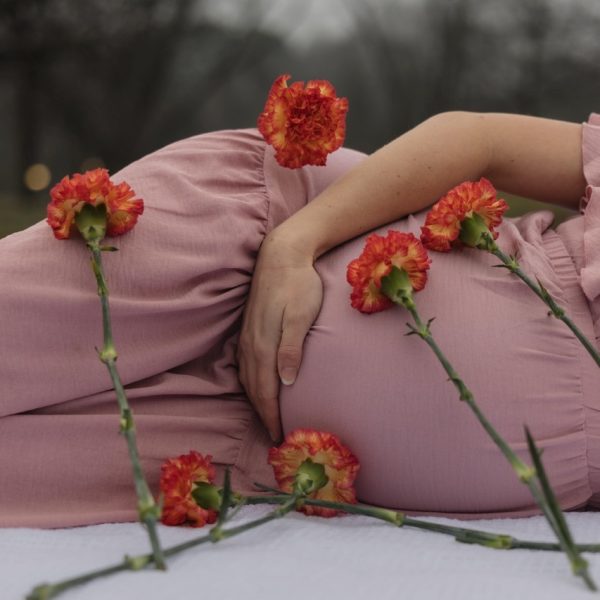 a pregnant mom laying on a blanket with pink and orange flowers laying around her in a stylized maternity photoshoot